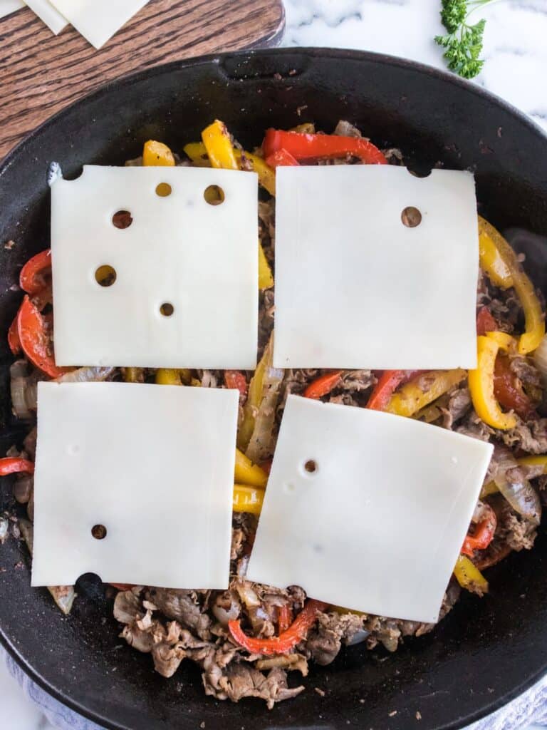 swiss cheese on top of beef, peppers, and onions