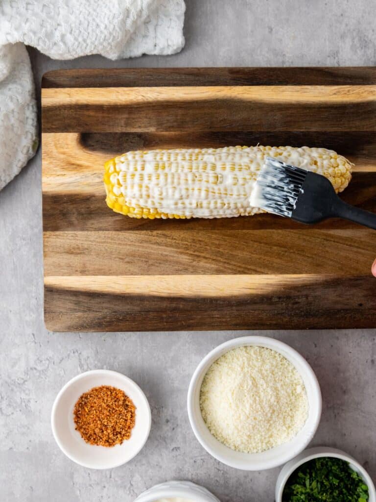 brushing corn on the cob with mexican crema mixture